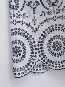Detail of floral geometric embroidery and scalloped hem on white cotton summer dress