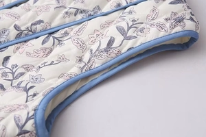 Close-up of quilted vest armhole with floral print and blue piped edge detail