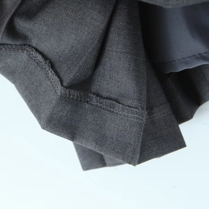 Macro detail of dark grey high-waist pleated skirt showing fine inner stitching and twill fabric