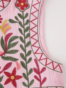 Detailed macro shot of ethnic floral embroidery on a pink Y2K style vest fabric