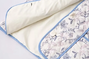 Close-up of quilted floral vest featuring sky blue piping and white round buttons