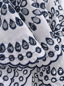 Close-up of white fabric featuring intricate navy blue floral embroidery and eyelet details