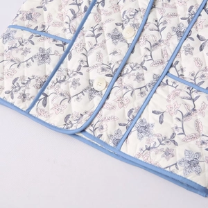 Detail view of quilted cotton vest featuring floral prints and blue contrast piping edges