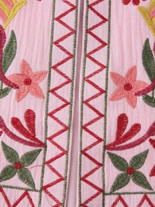 Close-up of ethnic Y2K style embroidery on pink textured fabric of a cropped vest