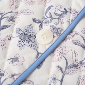 Close-up of diamond quilted fabric with floral print, ivory button and blue piping detail