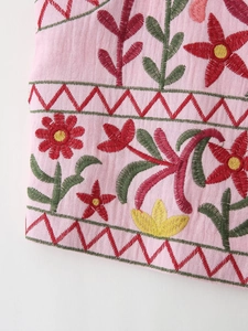 Detailed close-up of colorful floral embroidery and textured woven fabric on pink vest