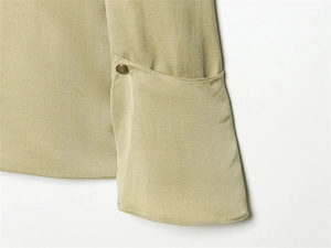 Detailed close-up of khaki blazer sleeve with vintage embossed metal button and flap