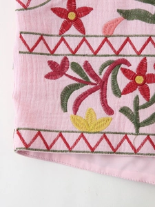 Detailed close-up of pink fabric with intricate floral embroidery and wavy red borders