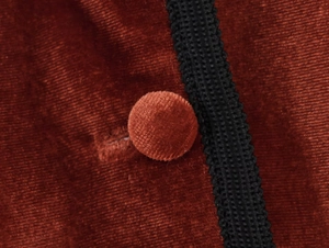 Detailed macro view of dark orange velvet fabric with a fabric-covered button and black trim