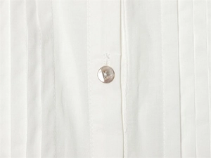 Close-up of pearl button and vertical pleats on a white cotton blouse detail