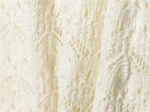 Close-up of ivory white knitted fabric with intricate floral hollow-out pattern