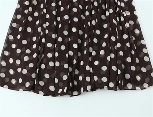 Dettaglio di tessuto in chiffon marrone a pieghe con pois bianchi e orlo delicato