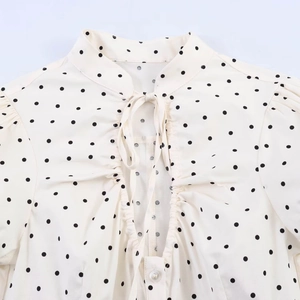 Detail of white polka dot poplin top featuring bow tie neckline and pleated hollow accents
