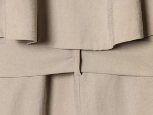 Detail of light khaki trench coat showing waist belt loops and layered fabric texture