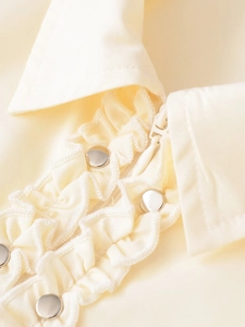 Détail de la chemise en popeline crème avec volants et boutons argentés à rivets