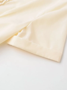 Détail macro du tissu satiné beige avec couture d'ourlet précise et éclat soyeux