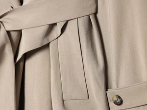 Macro shot of khaki trench coat featuring amber button and tied waist belt details