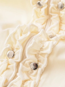 Détail d'une chemise en popeline crème avec boutons cloutés et bords à volants