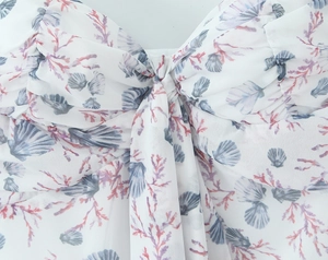Detailed view of women's floral dress featuring shell prints and a stylish knotted chest tie