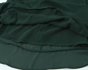 Détail de l'ourlet de robe vert foncé montrant la couture surjetée et le tissu mousseline