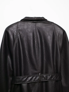 Detail view of the back of a deep brown faux leather coat with grain texture and waist belt