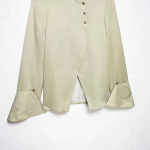 Pale green blazer with bell cuffs and asymmetrical layered design on white background