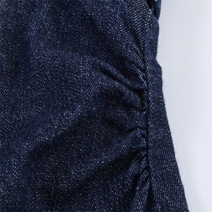 Gros plan sur la texture du denim bleu foncé avec des neps blancs et des détails de couture plissés