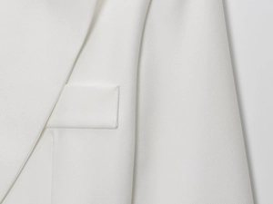 Close-up of white linen blazer showing twill fabric texture and pocket stitching