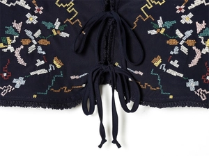 Close-up of multicolored floral cross-stitch embroidery and lace-up details on blue top