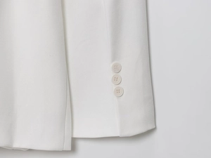 Macro view of white linen blazer sleeve featuring three matching buttons and twill texture