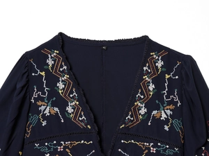 Close-up of navy V-neck top with floral cross-stitch embroidery and tassel trim detail