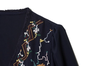 Detail of navy top featuring V-neckline with tassel trim and floral cross-stitch embroidery