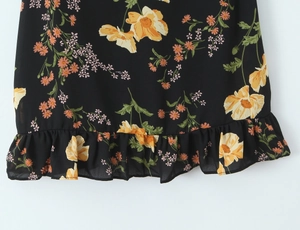 Detail of floral printed hemline with ruffled edges on a slim fit black sundress