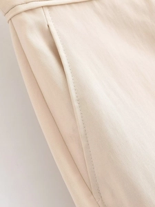 Détail du pantalon large beige montrant les plis à la taille, la poche et les coutures
