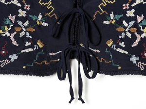 Detail of colorful floral embroidery and tie-up closure on dark blue cropped top vest