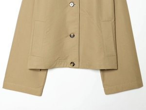 Detailed flat lay of khaki short trench coat featuring large utility pockets and horn buttons