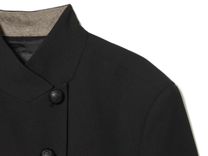 Detail of high-collared black blazer featuring textured fabric and grey plaid lining