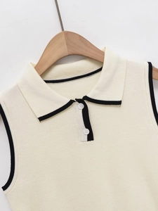 Close-up of cream knit polo vest with black contrast piping and white button detail