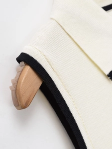 Detailed close-up of a cream knit top with contrast black piping on the polo collar
