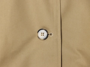 Close-up of a textured round button and fine double-stitched khaki trench coat fabric