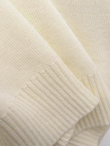 Detailed view of the fine rib-knit texture and soft cream fabric on sleeveless sweater