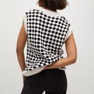 Detail view of the black and white checkerboard knit vest with ribbed hem and cuffs