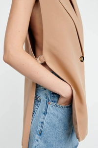 Detail of tan longline vest with side slits and metal ring buckle on textured fabric