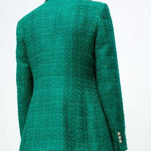 Detail of emerald green tweed blazer featuring elegant golden embossed buttons on sleeve