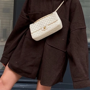 Close-up of white quilted leather flap bag with gold chain strap on shoulder