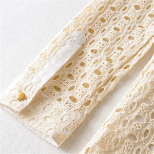 Detail der cremefarbenen Spitzenmanschette mit Lochstickerei und gelbem Harzknopf