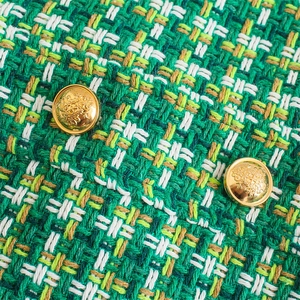 Dettaglio della trama in tweed verde con bottoni dorati decorativi su un abito gilet