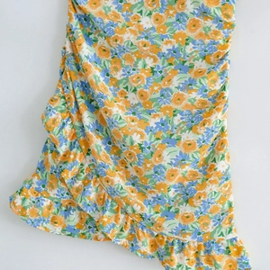 Detail view of floral print dress featuring orange roses and elegant side ruffles