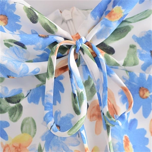 Détail du col en V avec imprimé marguerites, nœud décoratif et fermeture invisible