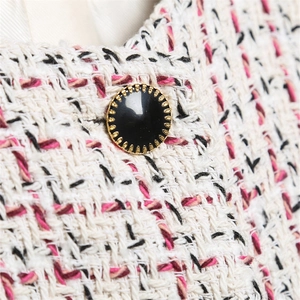 Close-up of pink and black tweed fabric texture with a decorative gold-trimmed button
